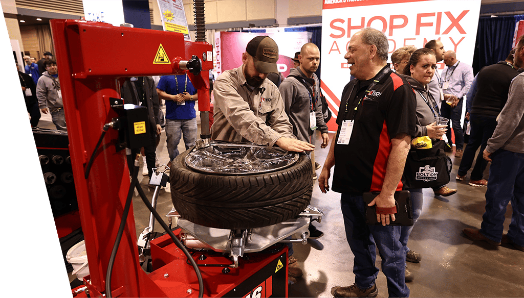 Interactive tire machine at VISION KC Expo - an attendee performing a tire change on a rim using machine at expo while vendor looks on